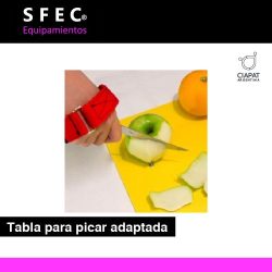En la imagen se muestra una tabla para picar adaptada, con clavos donde se pueden pinchar los alimentos, con manzanas y naranjas encima y una persona cortando.